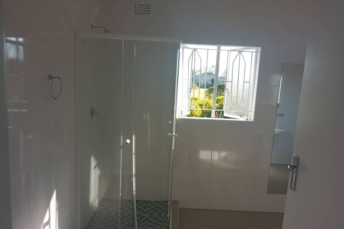 A shower with a glass door, a window with metal bars, and a view of greenery outside.