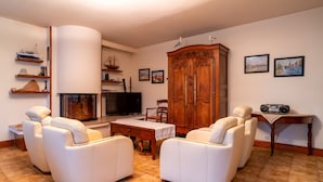 A living room with a TV, wooden cabinet, and two white leather sofas.