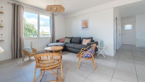 Ein modernes Wohnzimmer mit grauem Sofa, Korbstühlen, einem runden Tisch und einer Pendelleuchte.
