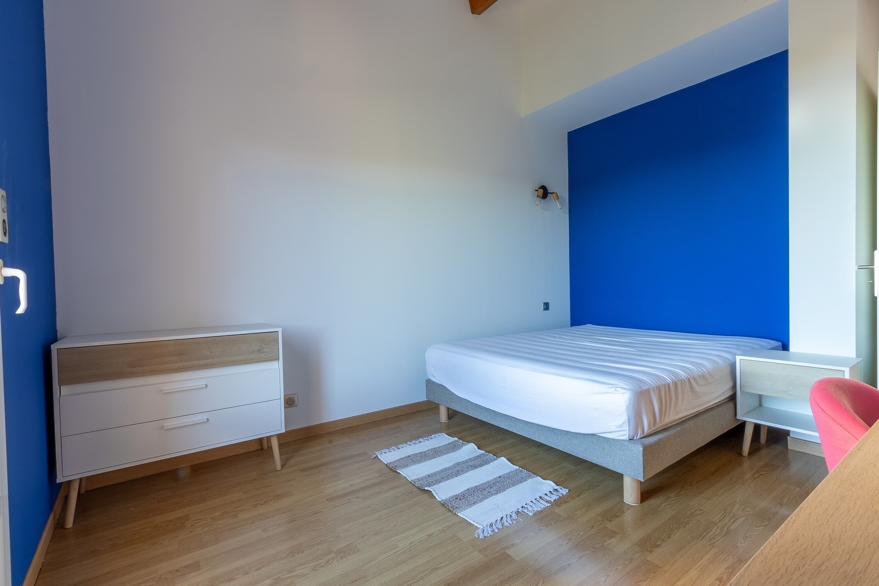 A bedroom with a bed, a nightstand, a dresser, and a window.