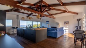 A modern kitchen with a central island, wooden beams, large windows, and a blue sofa in a bright living area. - L'Orangeraie de Portigliolo - Vue mer, 4 chambres (Coti-Chiavari)