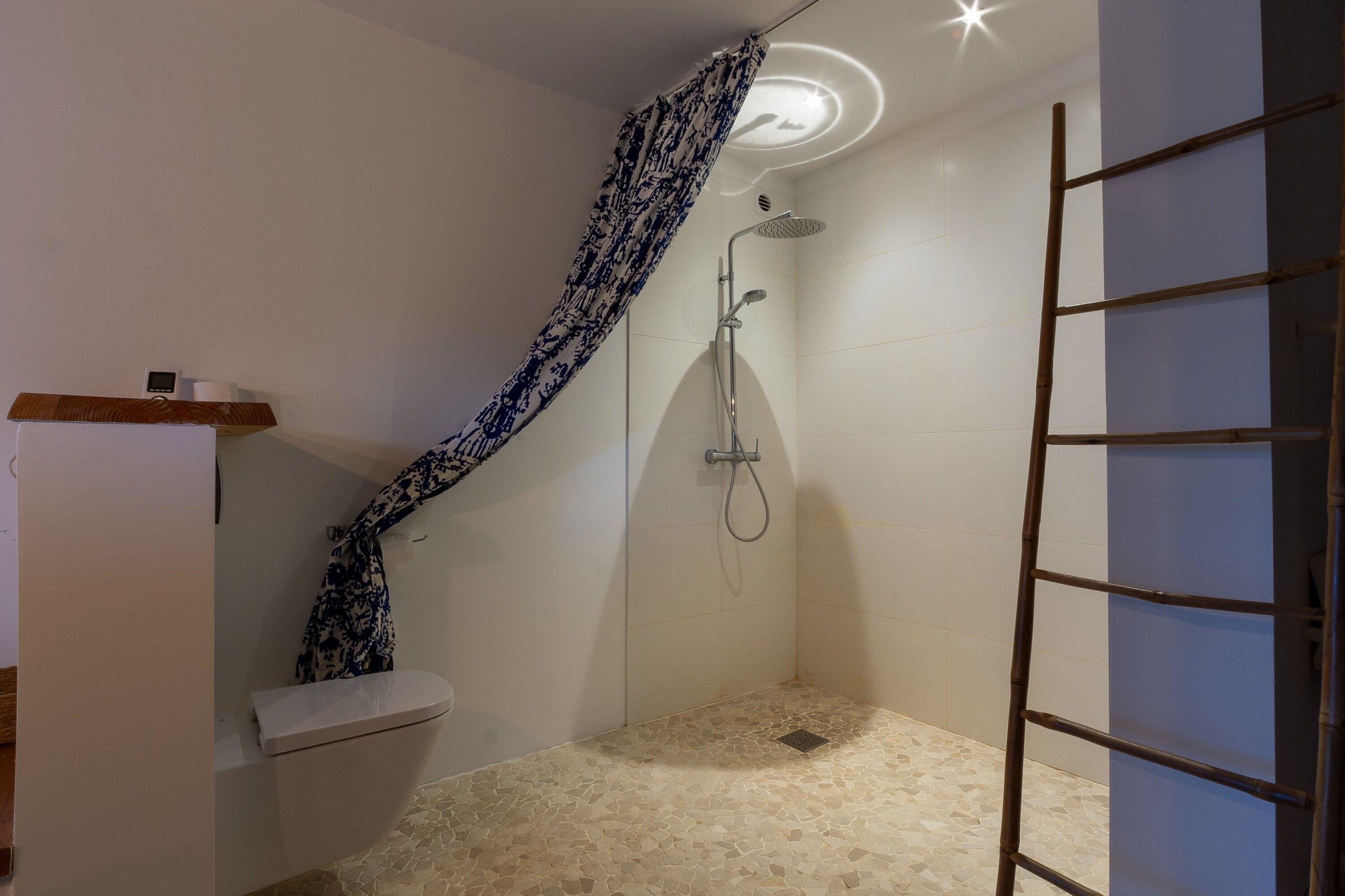 Un baño pequeño con ducha, inodoro y estante de madera.
