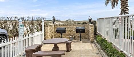An outdoor patio area with stone flooring, a white picket fence, and a view of the beach.