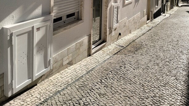 Uma rua de paralelepípedos com edifícios que apresentam fachadas brancas, portadas e sacadas.