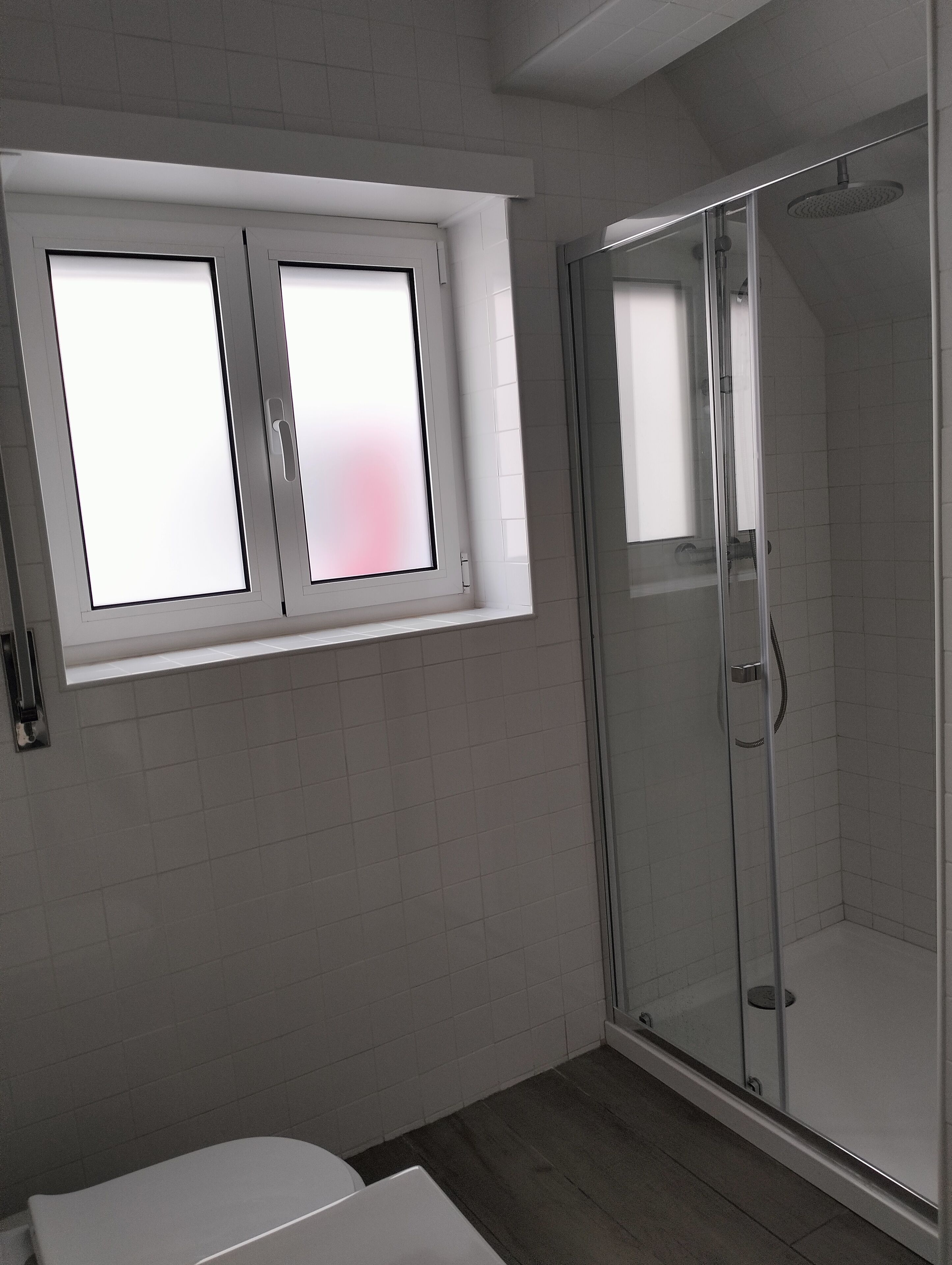 Een moderne badkamer met een douche, toilet en een raam.