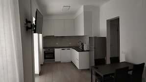 Cozinha moderna com armários brancos, micro-ondas e geladeira. Há uma área de refeições com mesa e cadeiras.