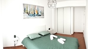 Quarto com cama verde, duas almofadas, um quadro na parede, um guarda-roupa branco e uma luminária geométrica.