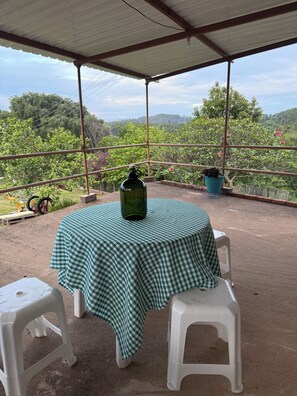 A covered outdoor area with a table and two chairs, a green bottle, and potted plants. - Sítio Aconchegante em Amparo/sp com uma Linda Vista Para Apreciar o pôr do sol (AMPARO)