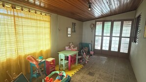 A spacious room with a high wooden ceiling, a large window with bars, a play area with toys, and a stone-tiled floor. - Sítio Aconchegante em Amparo/sp com uma Linda Vista Para Apreciar o pôr do sol (AMPARO)