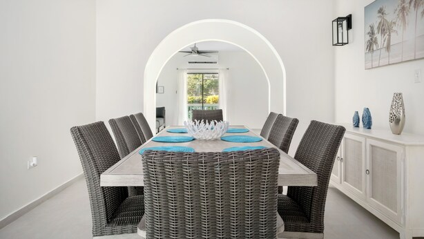 A dining area with a long table, wicker chairs, and a white cabinet. - Spacious Home with pool, steps from the beach in Puerto Rico! (Vega Alta)