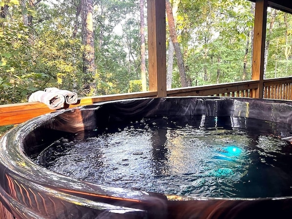 A hot tub with a wooden deck and a view of a forest.