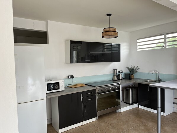 Une cuisine moderne avec des meubles de rangement noirs et blancs, un four encastré, un four à micro-ondes, un évier et un luminaire suspendu.