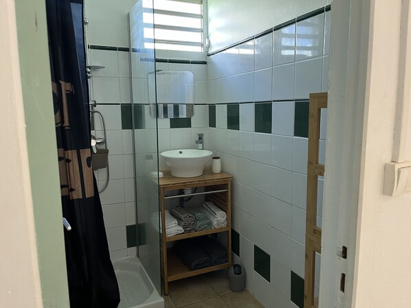 Ein Badezimmer mit einem weißen Waschbecken, einer Duschkabine aus Glas und einem Holzboden mit Handtüchern.