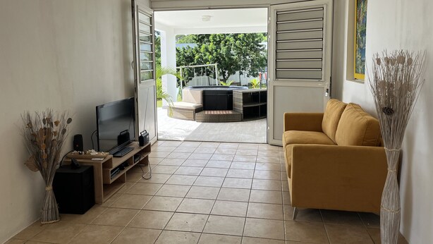 En stue med fjernsyn, sofa og balkon med udendørs møbler.