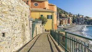 A cobblestone path leading to a yellow building with a round window, overlooking a beach with buildings in the background. - Apartment in Sori with 3 bedrooms sleeps 6 (Sori)