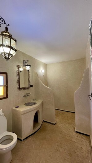A bathroom with a sink, toilet, and a mirror with wall-mounted lights. - Kasbah erg chebbi (Taouz)