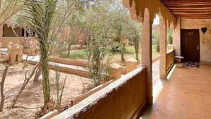 Un pasillo interior con techo de madera y vista a un área exterior con palmeras y un edificio.