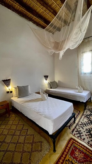 A room with two beds, a patterned rug, and a canopy bed. - Kasbah erg chebbi (Taouz)