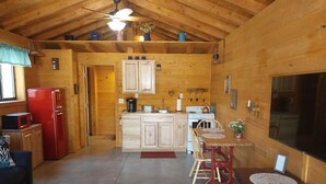 A cozy cabin interior with wooden walls, a kitchen area with a stove and cabinets, a dining table with chairs, and a red refrigerator. - Miners Cabin - New Private and Cozy (Cottonwood)