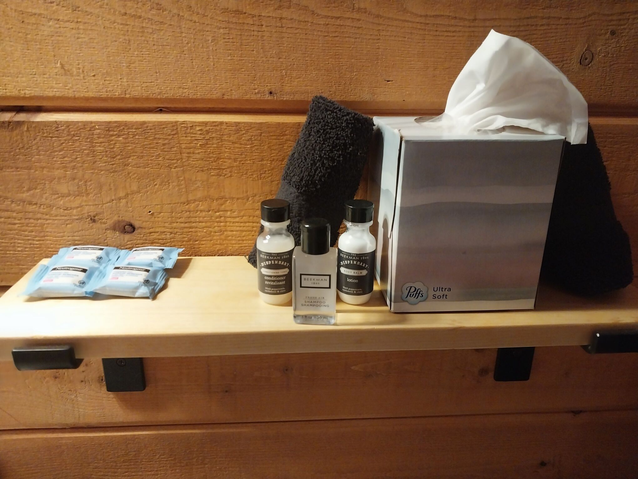 Eine Holzbank mit einer Taschentuchbox, zwei Lotionflaschen und einer Shampoo-Packung.