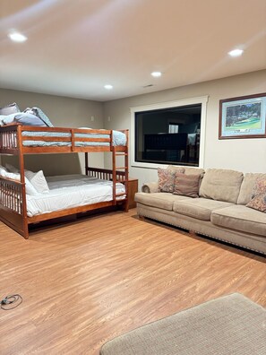 A bunk bed with a ladder, a sofa, a window, and a framed picture on the wall.