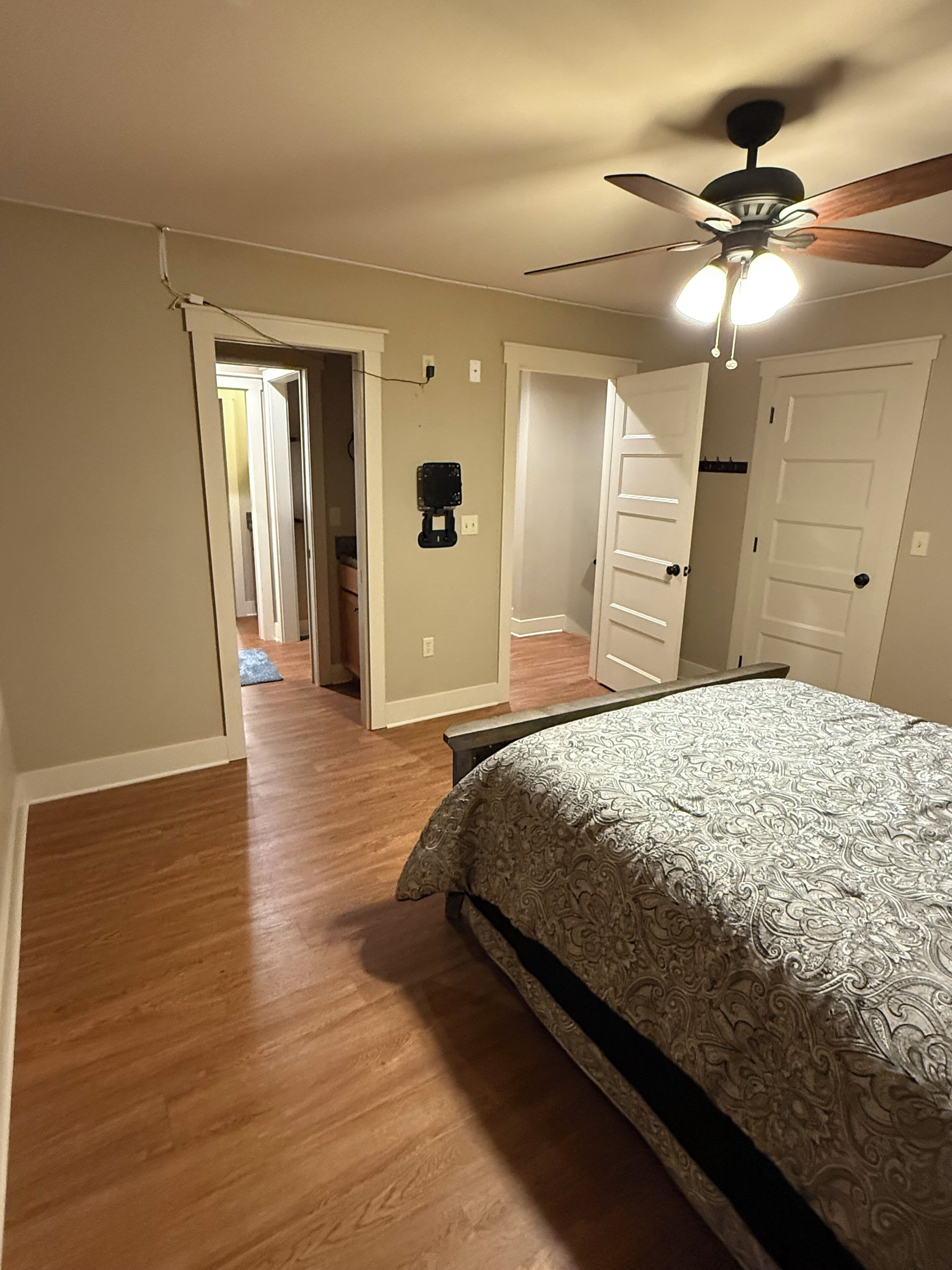 A bedroom with a bed, a ceiling fan, and a hallway leading to other rooms.