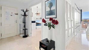 A modern hallway with a white door, a coat rack, a black side table with a vase of red roses, and a framed picture on the wall. - Torreblanca with pool by Costarentals - Ref 63 (Fuengirola)