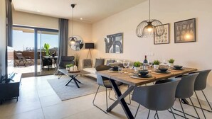 A modern dining area with a large table set for six, surrounded by black chairs. There is a sofa and a dining table with a view to the outside. - La Cala de Mijas Modern Flat with Pool - ref 240 (Las Lagunas de Mijas)