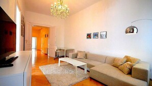 Ein modernes Wohnzimmer mit einer Couch, einem Couchtisch und einer Chandelier. An der Wand befinden sich gerahmte Bilder und eine Tür zu einem anderen Raum.