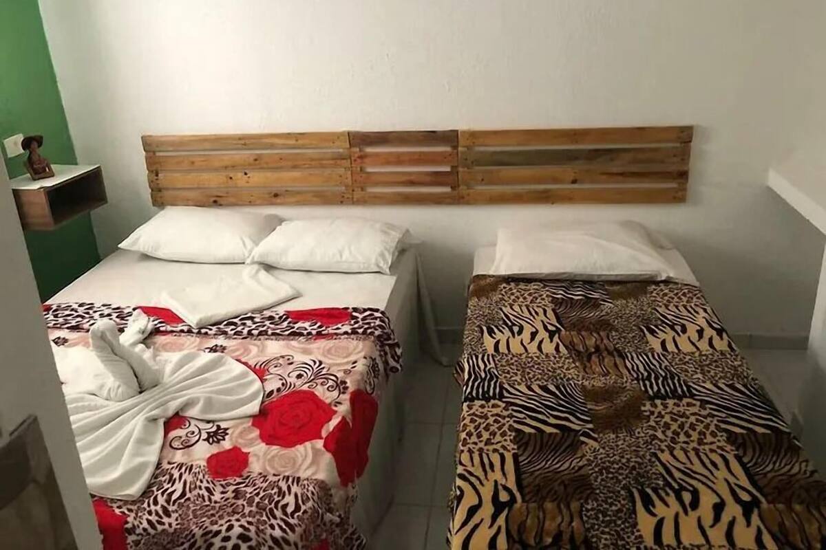 A room with two beds, each with a wooden headboard. The beds have patterned bedspreads, one with a floral design and the other with a zebra print.
