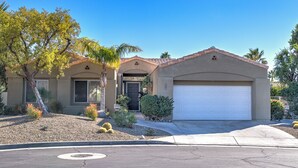 A two-story house with a garage, a well-maintained front yard with cacti and shrubs, and a clear blue sky. - The Desert Flower, designer home in gated community/ private pool and jacuzzi. (Palm Springs)