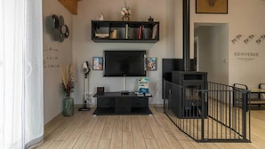 A living room with a TV, black shelves, a fireplace, and a 'BIENVENUE' sign.