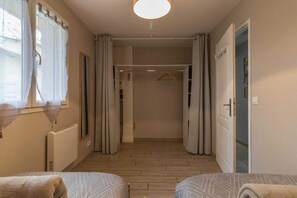 Une chambre à coucher comprenant un lit, un radiateur, une fenêtre avec des rideaux et une porte donnant sur une salle de bain.