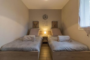A bedroom with two beds, a clock on the wall, and a window with curtains.