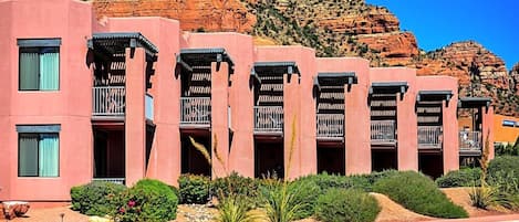 A row of pink buildings with balconies, set against a rocky mountain backdrop.