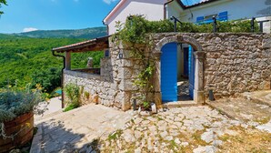 A stone house with a blue door, a stone wall, and a view of green hills. - Villa Eugenia (Kvarner - Mošćenička Draga) (Mošćenička Draga)
