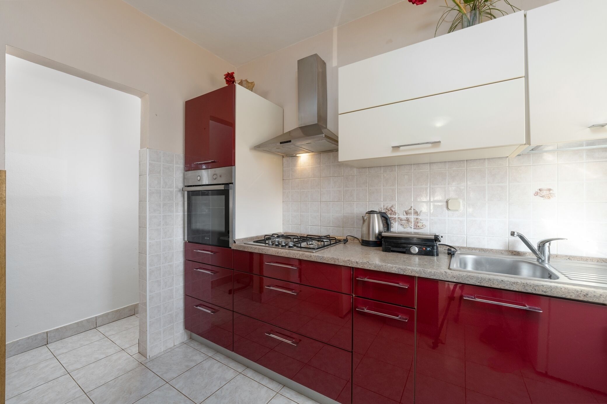 A kitchen with red cabinets, a stainless steel range hood, a gas stove, and a sink.