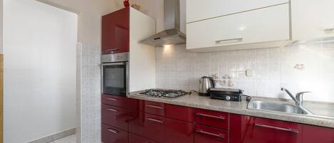 A kitchen with red cabinets, a stainless steel range hood, a gas stove, and a sink.