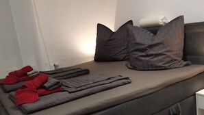 A modern, dark grey sofa bed with a grey blanket and red towels.