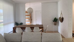 A modern living room with a sofa, a dining table with chairs, a hanging light fixture, and a white brick wall. - Rye Beach Escape (Rye)