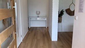 A hallway with wooden flooring, a white console table with decorative items, and a white brick wall with hanging decorations. - Rye Beach Escape (Rye)