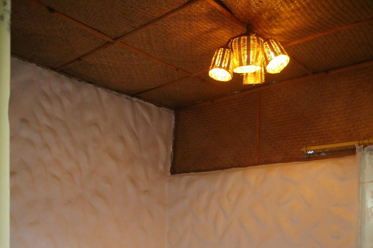 A hotel room with a bed, pillows, a wooden headboard, a textured wall, and a hanging light fixture.