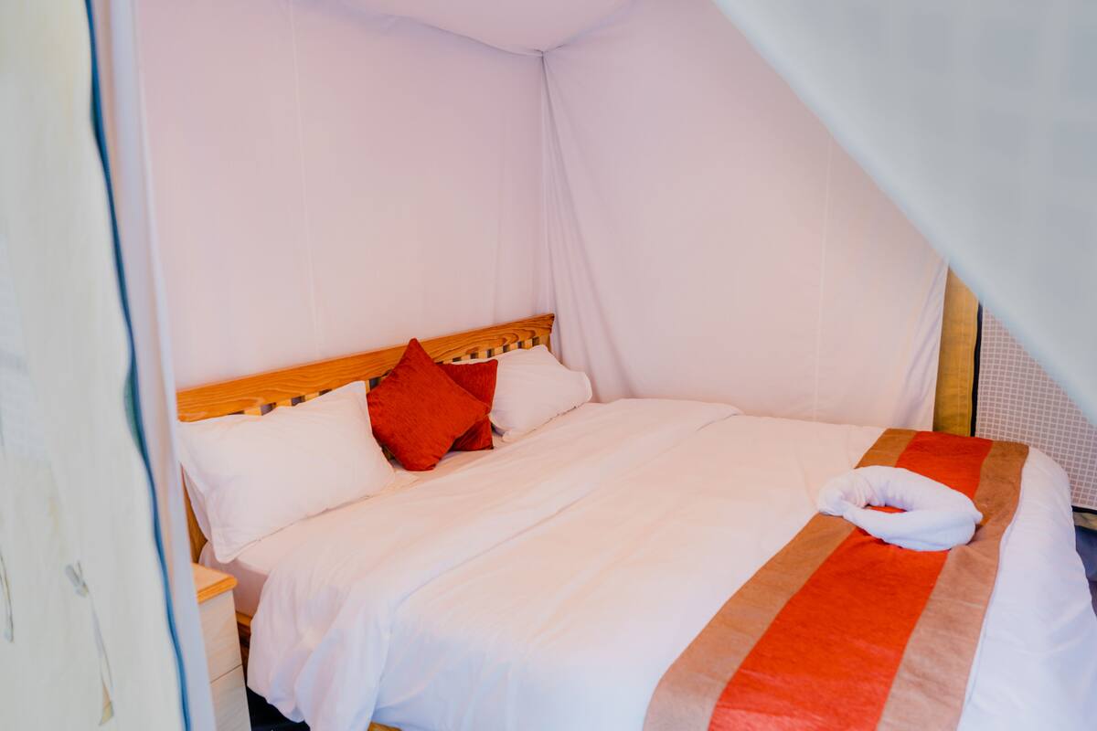 A neatly made bed with white and red bedding, a wooden headboard, and a white pillow on the bed.