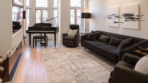 A living room with a grand piano, a sofa, a chair, and artwork on the wall. - Villa Montcalm: Prestige & Confort au Vieux-québec (Québec)