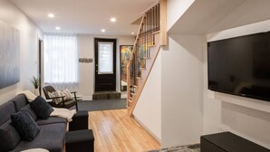 A modern living room with a sofa, ottoman, and a flat-screen TV. - Villa Montcalm: Prestige & Confort au Vieux-québec (Québec)