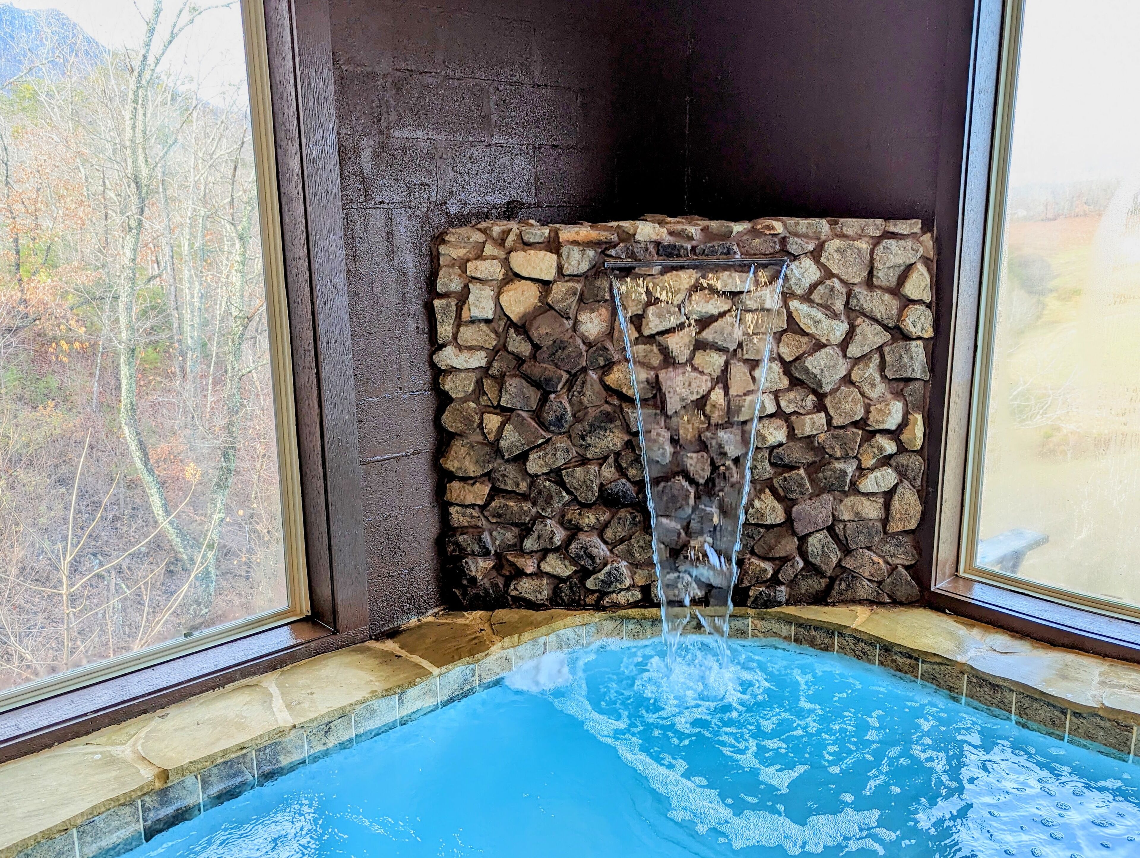Een stenen muur met een waterval in een zwembadgedeelte.