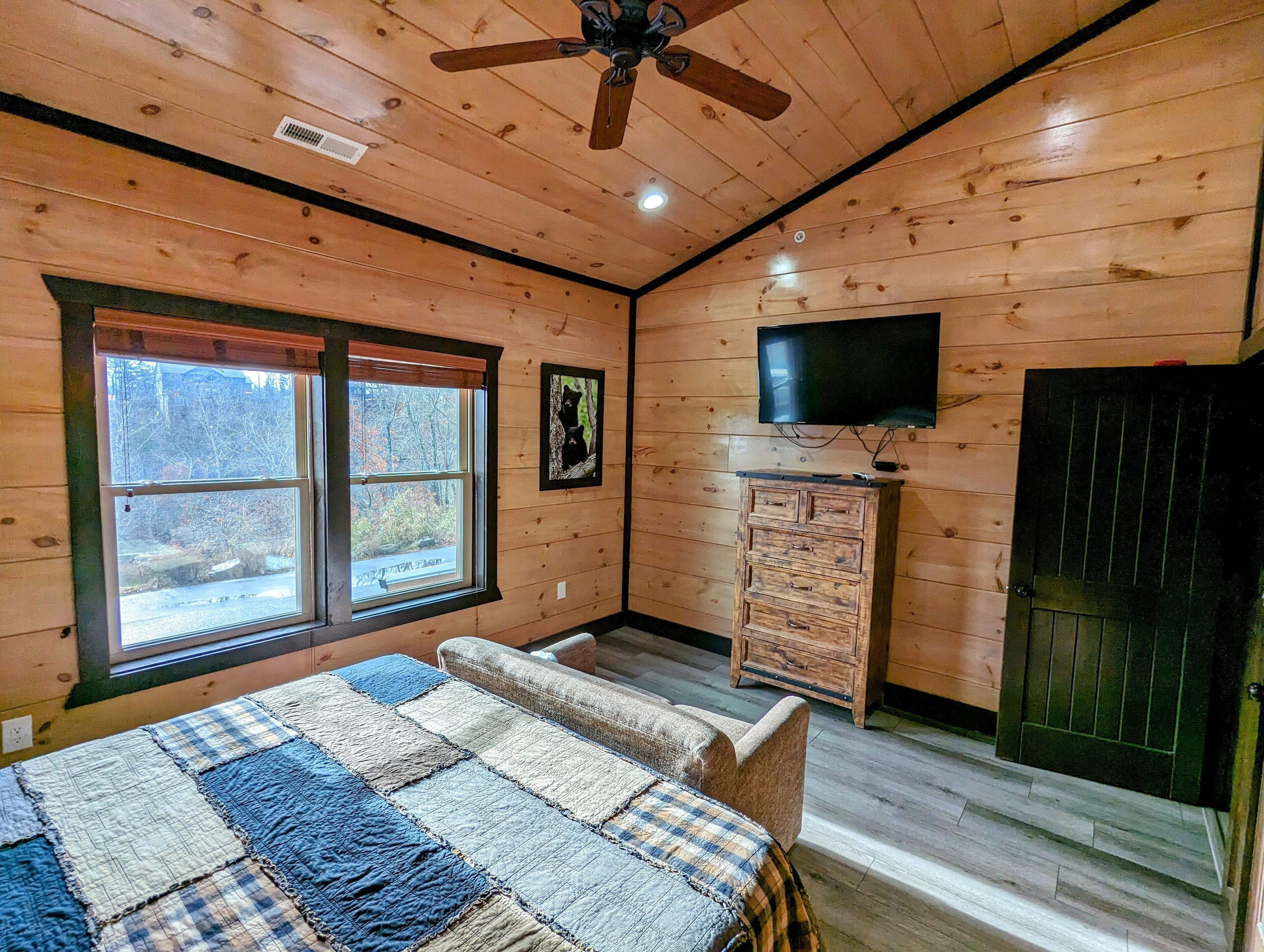Una habitación tipo cabaña acogedora con un ventanal grande, un televisor, un aparador de madera y una colcha acolchada.