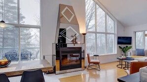 Una sala de estar moderna con chimenea, ventanas amplias y una zona de comedor.