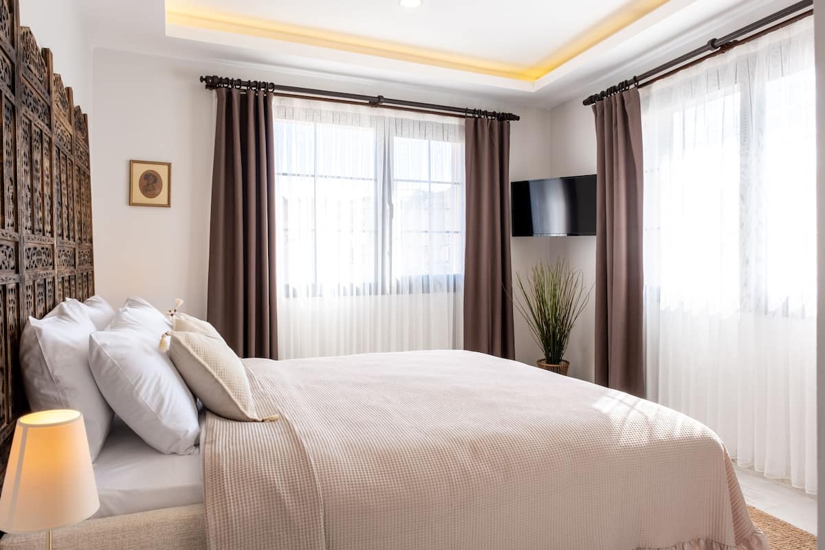 Un dormitorio ordenado con una cama grande, un televisor de pantalla plana y una ventana con cortinas.