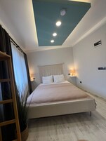 A modern bedroom with a bed, bedside lamps, a ceiling light, and a macrame wall hanging.